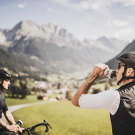 Two bikers are drinking from their water bottles
