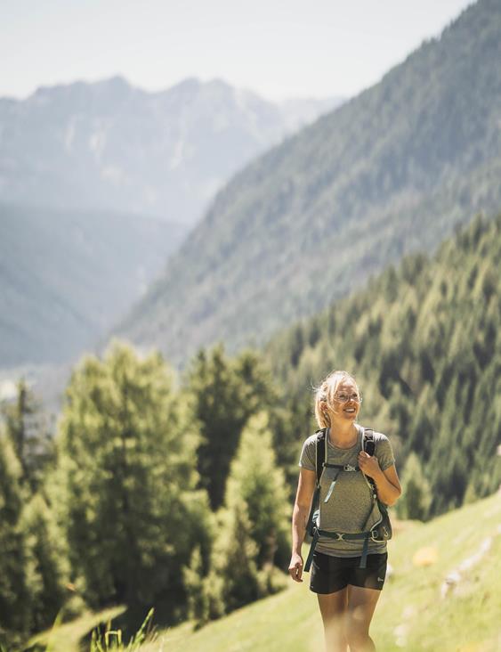 A smiling woman with a hiking backpack is standing on an alpine meadow