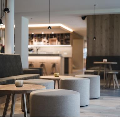Unsere modern eingerichtete Hotel-Lounge mit runden Hockern, Holztischen und gedämpfter Beleuchtung; im Hintergrund unsere stilvolle Bar