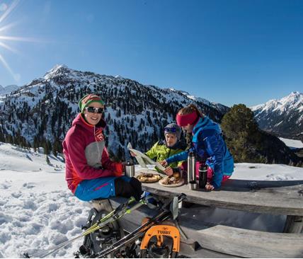 Drei Wintersportler genießen eine Jause im Freien