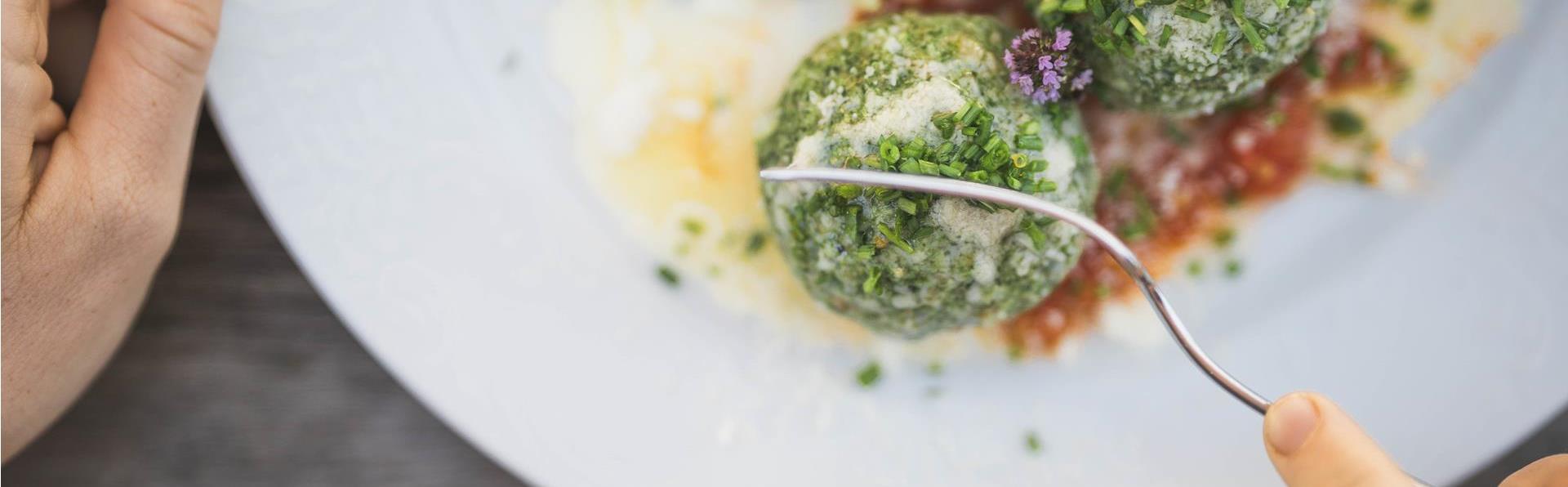 Eine Person zerteilt einen Spinatknödel mit der Gabel