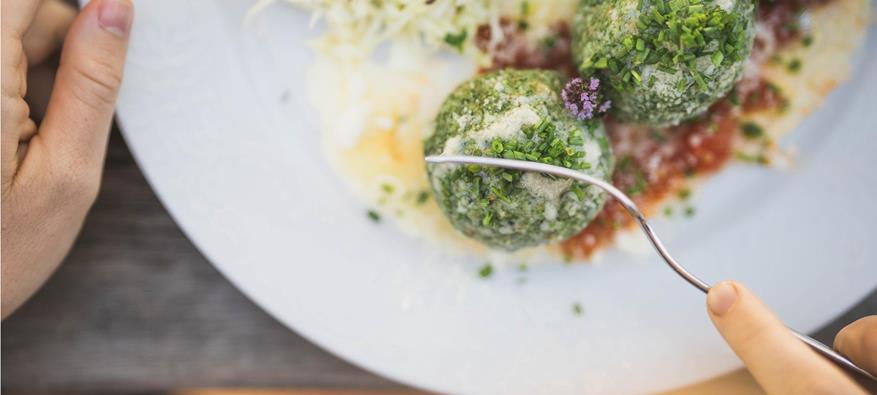 Eine Person zerteilt einen Spinatknödel mit der Gabel