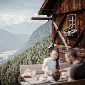 A family is having a meal at the Kumpflalm with view on the mountains and the valley