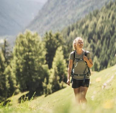 Eine lächelnde Frau mit Wanderrucksack steht in einer Alpenwiese