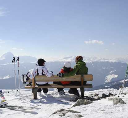 Tre persone seduti su una panchina si godono la vista sulle montagne invernali