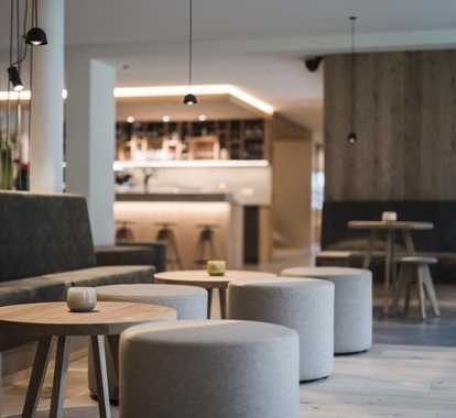 Our modern hotel lounge with round stools, wooden tables, and soft lighting; in the background, our stylish bar with high stools